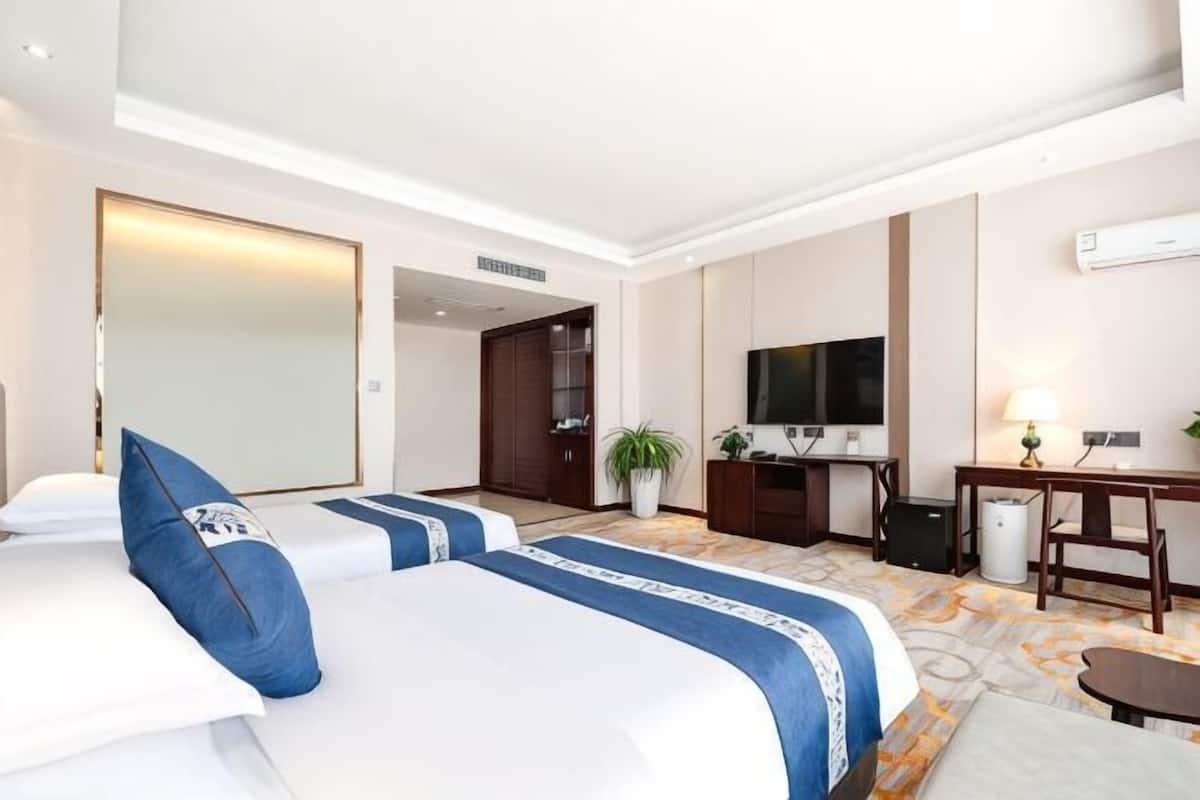 A hotel room with two beds, a TV, a desk, and a mirror.