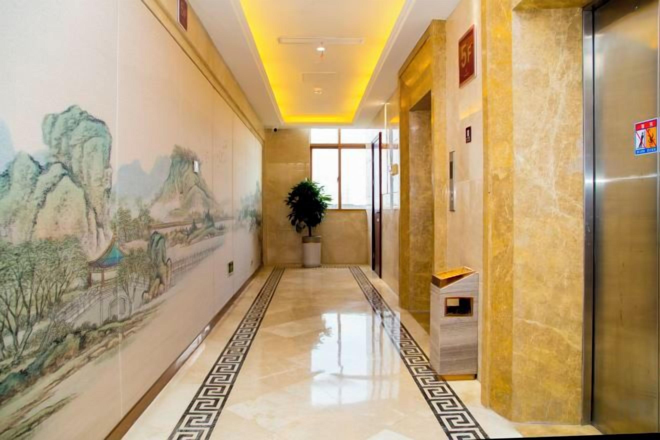 A hallway with a mural, a potted plant, and an elevator.