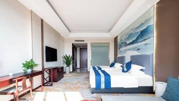 Habitación de hotel con cama, escritorio, televisión, planta y un cuadro en la pared.