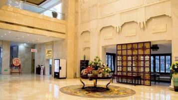 A spacious lobby with a high ceiling, a reception desk, and a decorative display of flowers.
