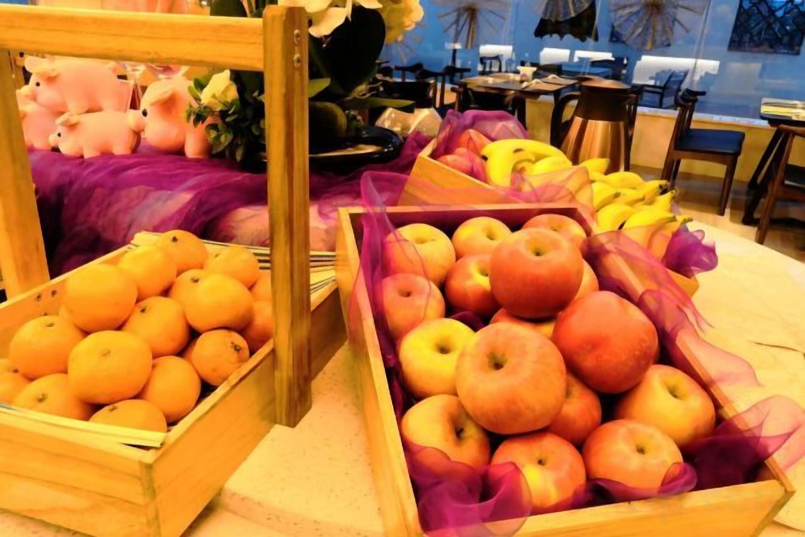 Frutas expuestas en cajas de madera, una cama con una colcha morada y un escritorio con una computadora.