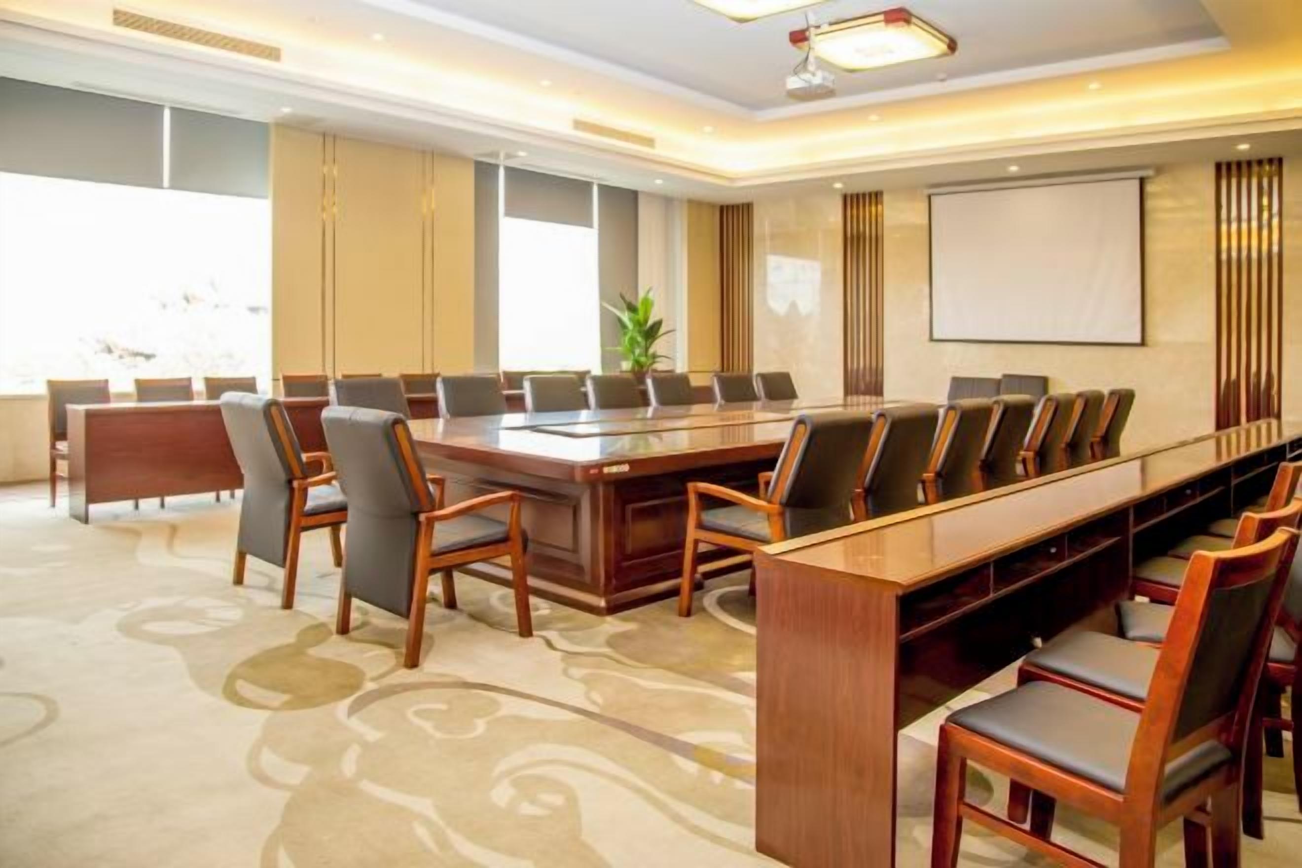 Una sala conferenze con un lungo tavolo e sedie, uno schermo per proiettore e una grande finestra.