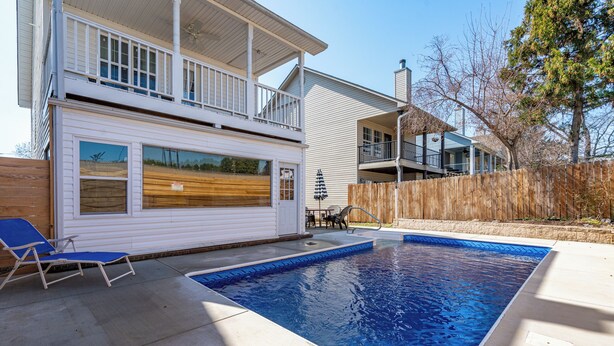 En swimmingpool i et boligområde med træterrasse, overdækket terrasse og en hegnet baghave.
