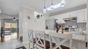 Et moderne køkken med hvide skabe, en marmor bordplade og et rustfrit stål køleskab.