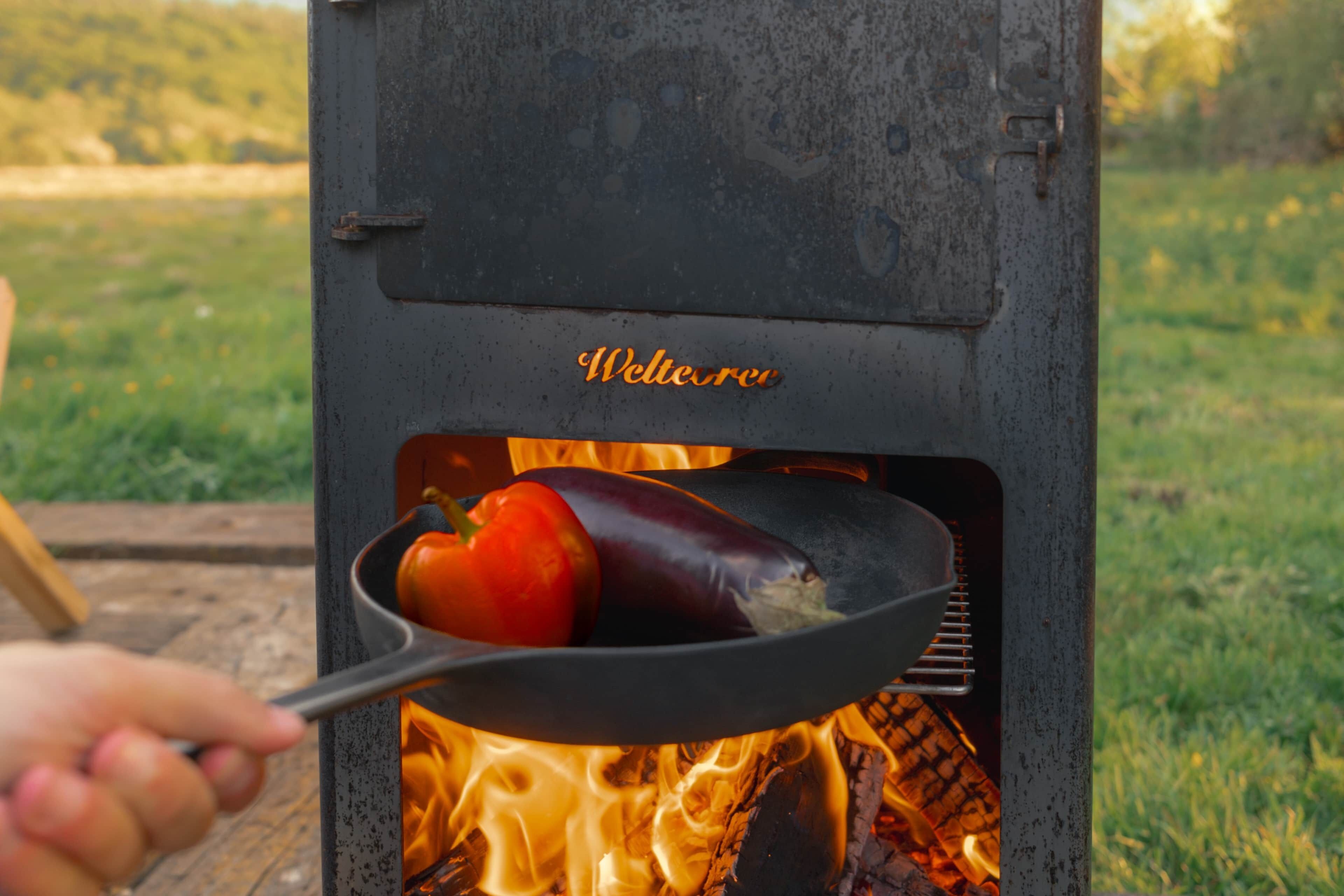 Un petit barbecue portable pour l’extérieur, doté d’un couvercle en métal et d’une poignée, et contenant un poivron rouge et une aubergine.