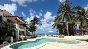 A pool area with a curved design, surrounded by palm trees and lounge chairs, with a view of the ocean.