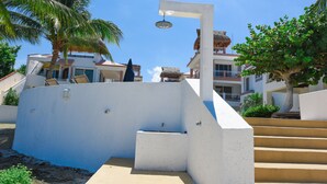A white building with a staircase leading to a balcony, surrounded by palm trees and other greenery.