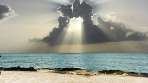 A beach with a clear sky and sunlight shining through clouds.