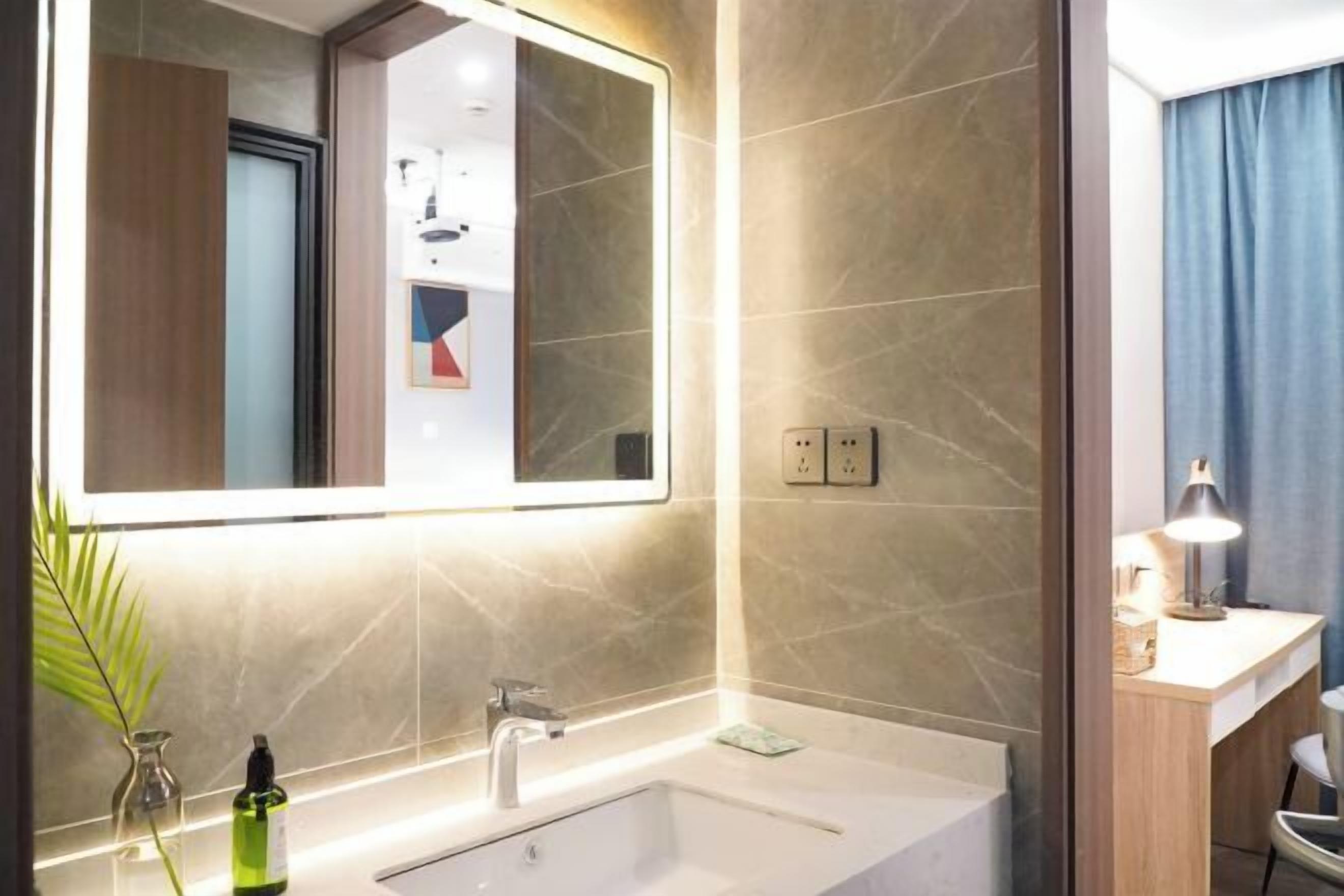 A modern bathroom with a large mirror, a bathtub, and a countertop with a lamp.