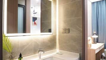 A modern bathroom with a large mirror, a bathtub, and a countertop with a lamp.