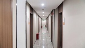 Un pasillo largo y estrecho con puertas a ambos lados, un cubo de basura en el centro y una fuente de luz en el techo.