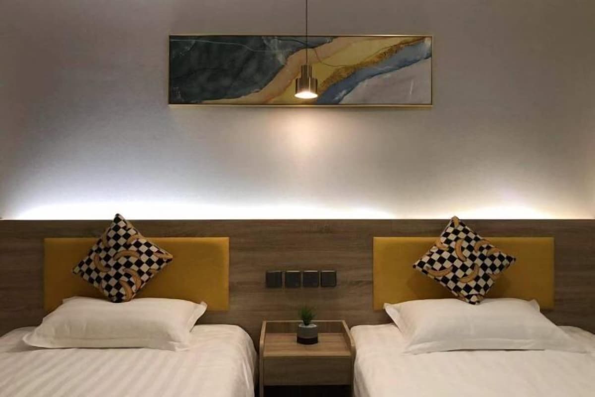 A hotel room with two beds, a headboard with a geometric pattern, a wall-mounted artwork, and a bedside table with a plant.