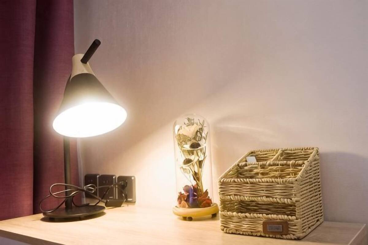 A desk with a lamp, a decorative glass vase, and a wicker basket.