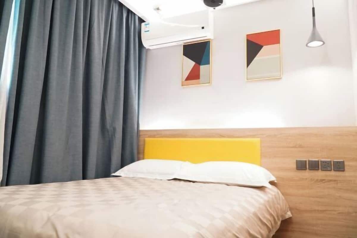 A hotel room with a bed, a headboard, a wall-mounted air conditioner, and two framed artworks.