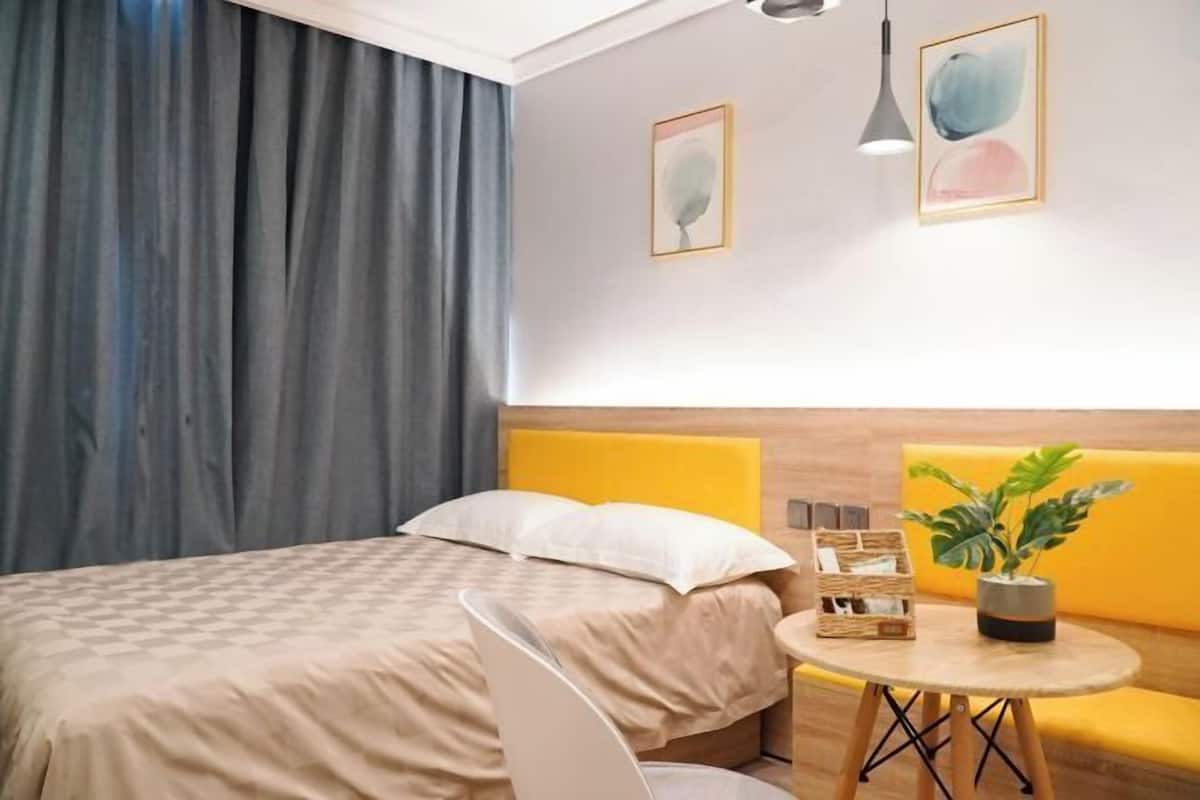 A hotel room with a bed, a round table with a plant, and two framed artworks on the wall.