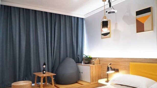 Una habitación de hotel moderna con cama, mesita de noche, lámpara, sillón de saco y un ventanal con cortinas.