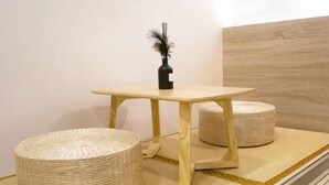 Una habitación con una mesa de madera, dos otomanes redondos tejidos y un florero negro con una pluma.