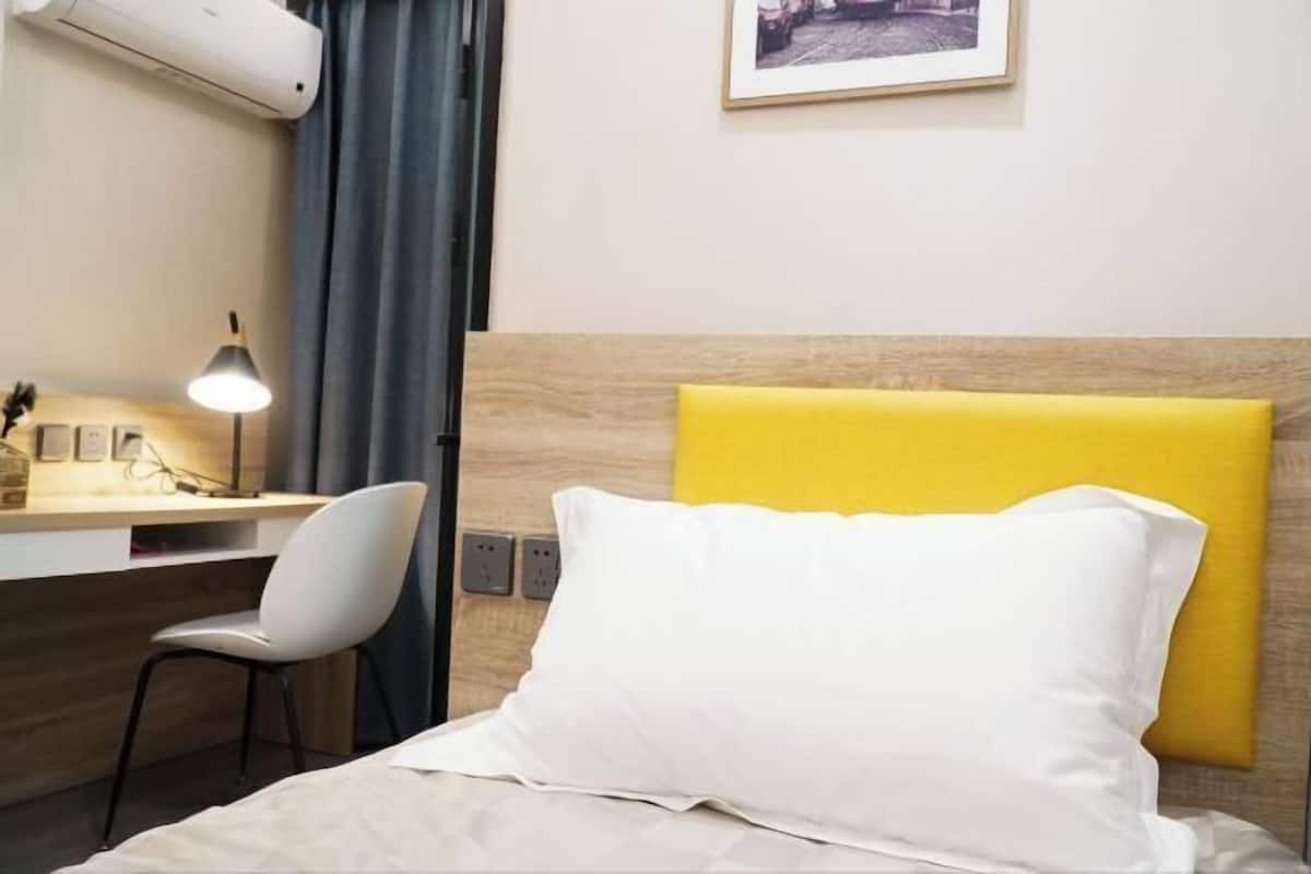 A hotel room with a bed, a desk, a chair, a lamp, and a picture on the wall.