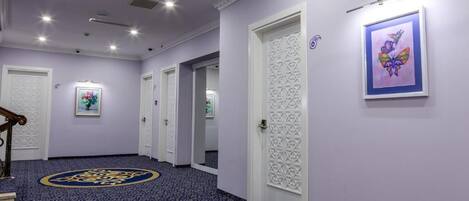 A hallway with patterned carpet, white doors, and framed artwork on the walls.