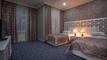 A hotel room with two beds, a TV, a nightstand with lamps, and a patterned carpet.