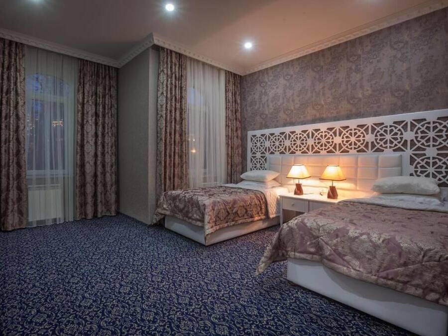 A hotel room with two beds, a TV, a nightstand with lamps, and a patterned carpet.