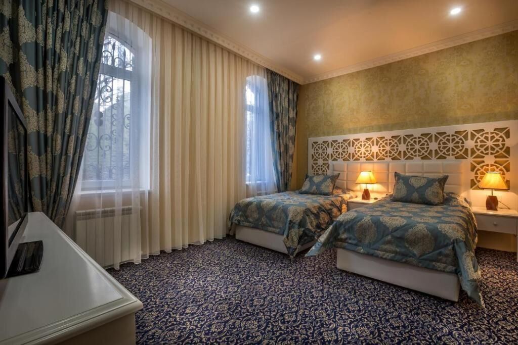 Een hotelkamer met twee bedden, een groot raam met gordijnen, een kamerbreed tapijt met een patroon en een decoratief wandpaneel.