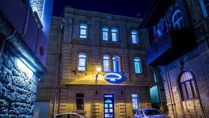 A building with a prominent illuminated sign, a cobblestone street, and two parked cars. - Seven Gates Boutique Hotel (Baku)
