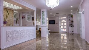 A hotel lobby with a reception desk, decorative columns, a chandelier, and a TV mounted on the wall. - Seven Gates Boutique Hotel (Baku)