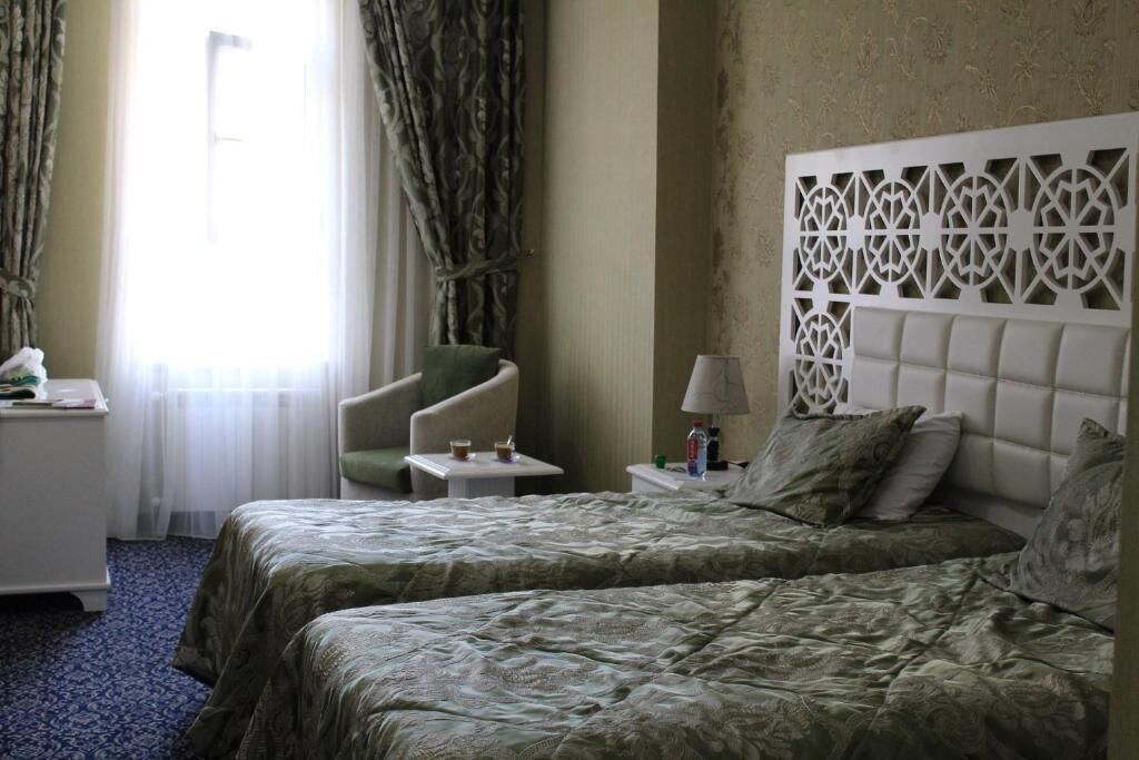 A hotel room with two beds, a chair, a nightstand, and a decorative headboard.