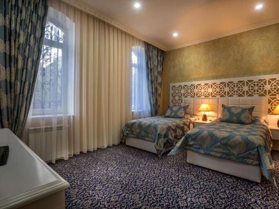 A hotel room with two beds, a large window with curtains, a patterned carpet, and a decorative wall panel.