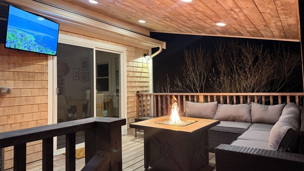 En træterrasse med ildsted, sofa og fjernsyn monteret på væggen.