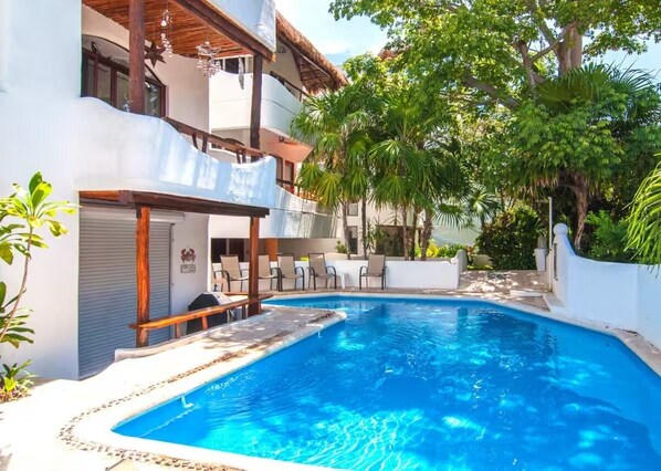 Una piscina con cubierta de madera, rodeada de paredes blancas y plantas tropicales.