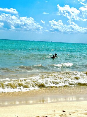 Una playa con agua turquesa cristalina, olas suaves y una orilla de arena.