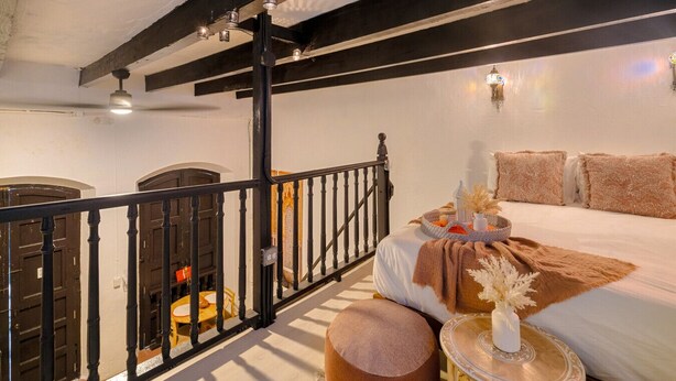 Een slaapkamer met een groot bed, een nachtkastje en een bijzettafeltje. Er is een balkon met een hekwerk en uitzicht op de omgeving.