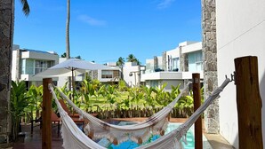 A hammock over a wooden deck with a pool, surrounded by palm trees and modern buildings. - MHV Milagres - Casa Naluum G4 (Passo de Camaragibe)