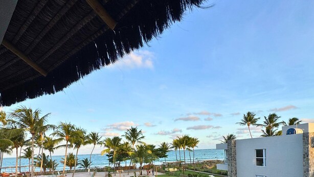 A pool area with a view of the ocean, palm trees, and a building with a stone facade. - MHV Milagres - Casa Naluum G4 (Passo de Camaragibe)