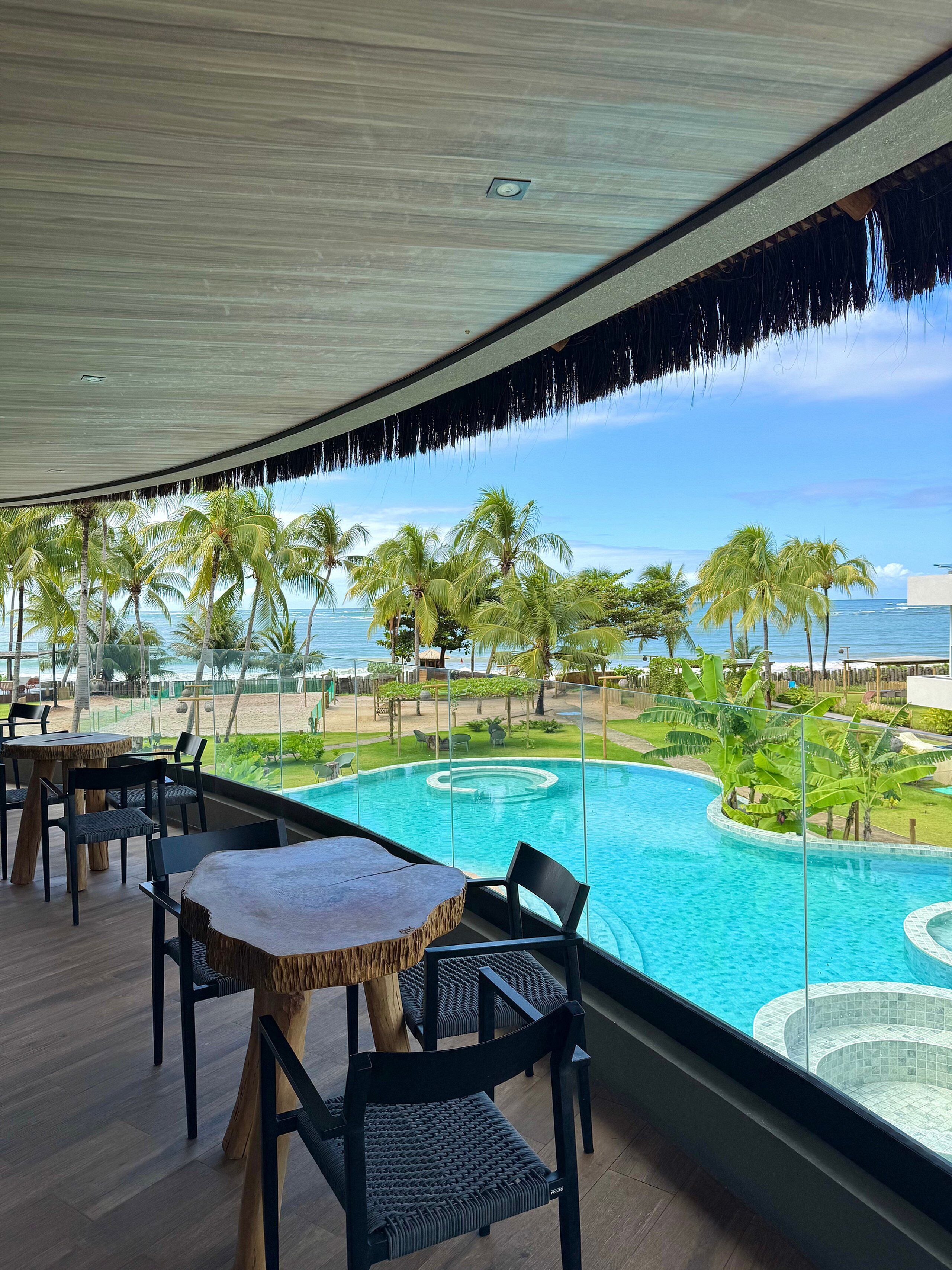 A poolside area with a view of the ocean, palm trees, and a circular hot tub.