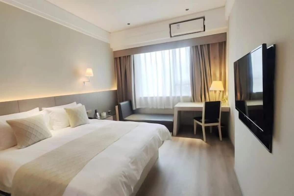 Een hotelkamer met een groot bed, een bureau, een stoel, een televisie en een raam met gordijnen.