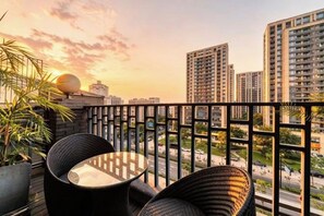 A balcony with wicker furniture, a potted plant, and a view of high-rise buildings during sunset. - Hanxiang Hotel (Hangzhou Wenyi West Road Branch University of Finance and Economics) (Hangzhou)