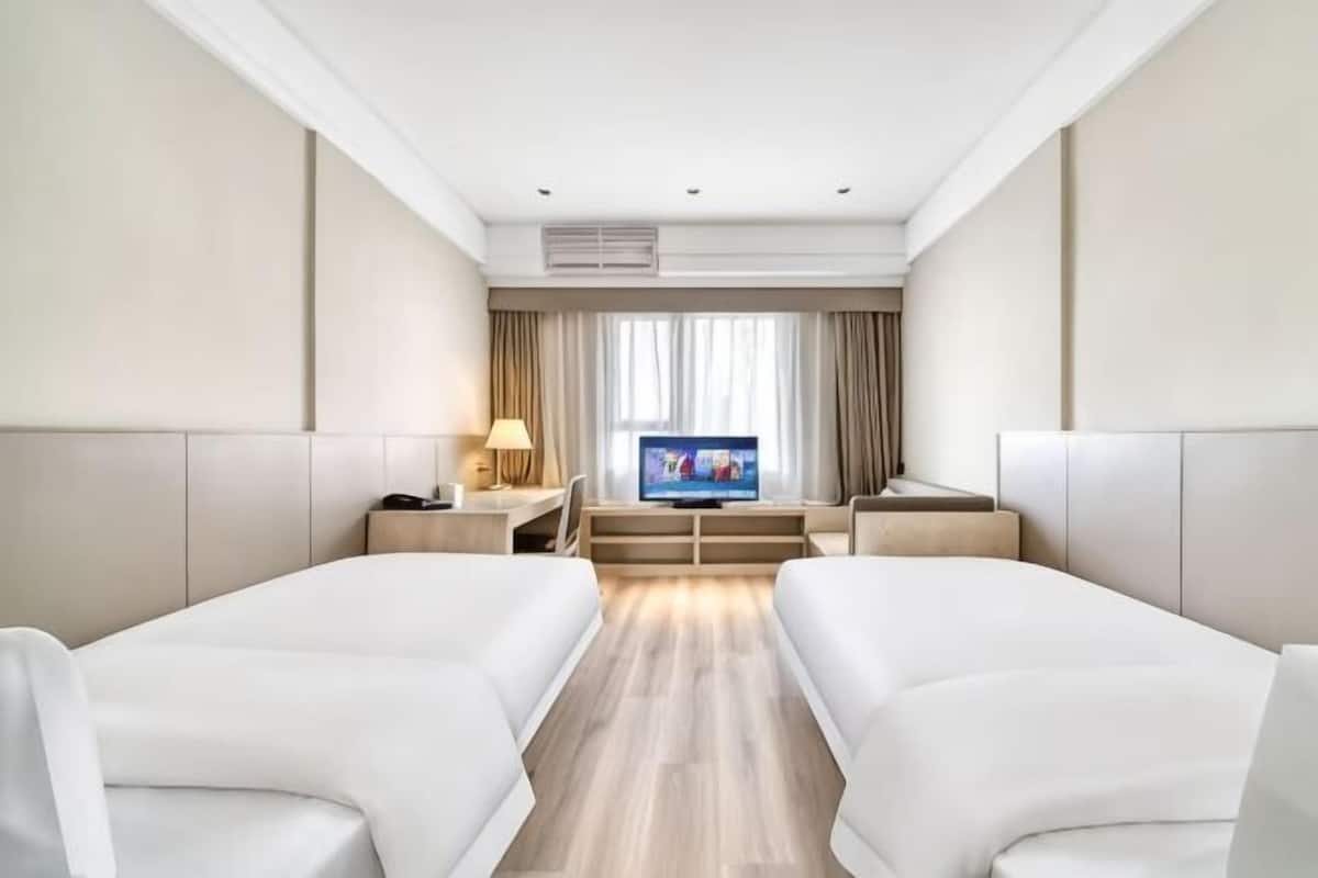Een hotelkamer met twee bedden, een televisie, een bureau en een raam met gordijnen.