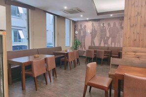 Ein Restaurant Innenraum mit Holztischen und -stühlen, großen Fenstern und einem Wandgemälde.