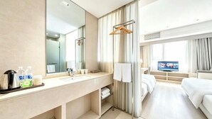 A hotel room with a large mirror, a sink, a television, a bed, and a window with curtains. - Hanxiang Hotel (Hangzhou Wenyi West Road Branch University of Finance and Economics) (Hangzhou)