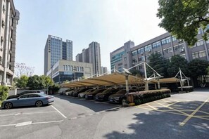 Un área de estacionamiento con aparcamiento techado y un edificio al fondo.