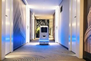 A corridor with a self-driving vehicle, a patterned carpet, and a door on the right. - Hanxiang Hotel (Hangzhou Wenyi West Road Branch University of Finance and Economics) (Hangzhou)