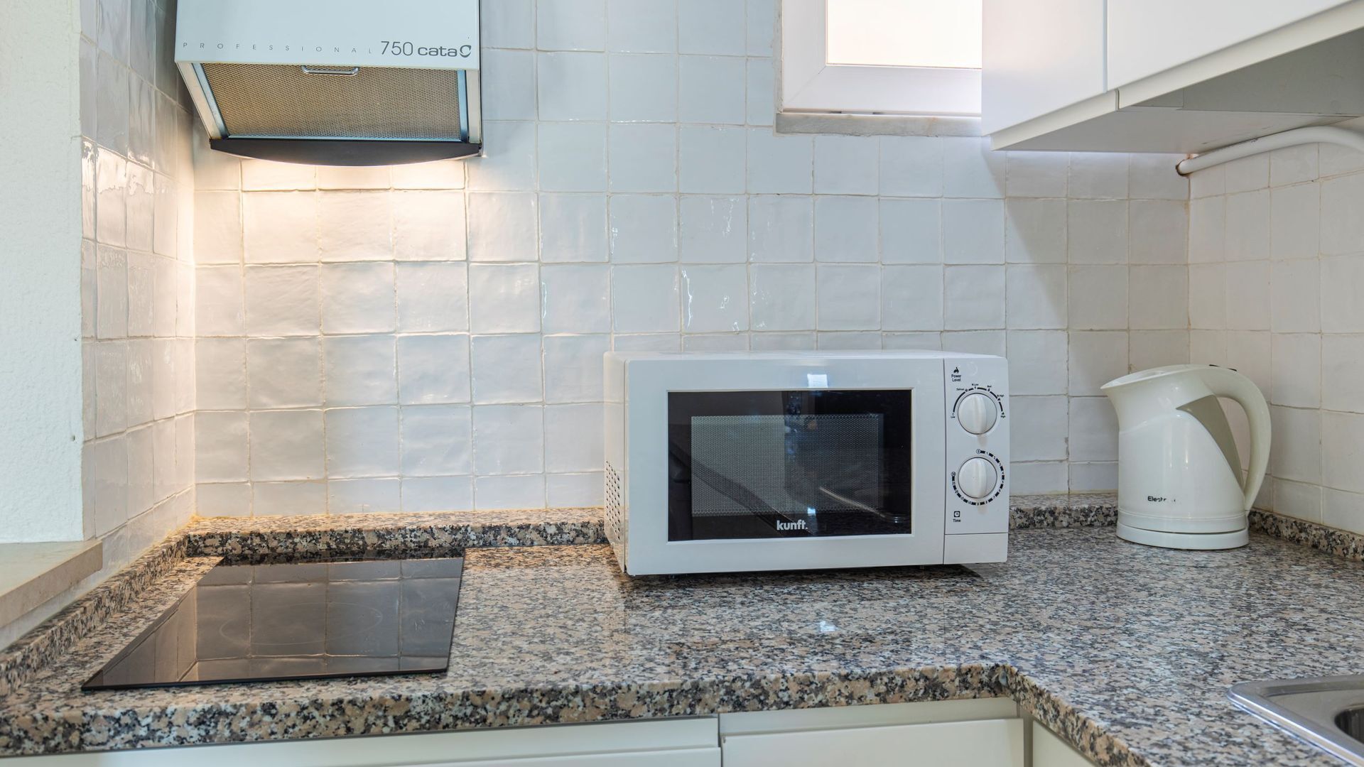 Een keuken met een witte magnetron, een waterkoker en een inbouwoven.