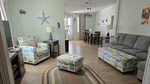 Een woonkamer met een bank, twee fauteuils en een salontafel, allemaal bekleed met een stof met een strandthema.
