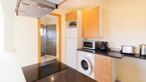 Cocina compacta equipada con microondas, tostadora, hervidor, lavadora y cabina de ducha de vidrio.