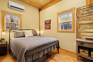 Quarto com cama, mesa de cabeceira, abajur e ar condicionado fixado na parede.