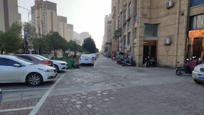 A street with parked cars and motorcycles, buildings on both sides, and a clear sky. - 7Days Inn Chain Hotel (Xuancheng High-Speed Railway Station) (Xuancheng)