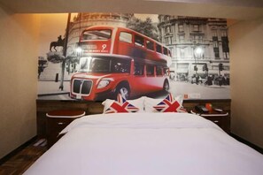A hotel room with a large bed, a small bedside table, and a wall-mounted artwork of a red double-decker bus.